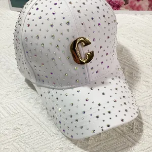 Dettaglio del cappello bianco con strass scintillanti e fibbia in metallo dorato a C