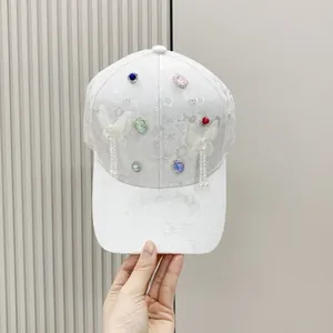 Detail of white lace baseball cap with butterfly decor, colorful gems and pearl tassels