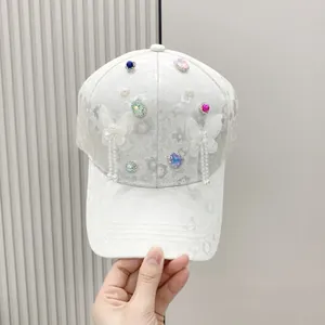 Detail of white baseball cap featuring lace floral texture, colorful rhinestones and butterfly tassels