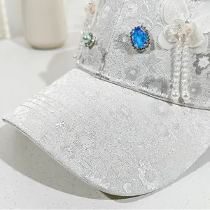 Detail of white lace baseball cap with blue gemstone butterfly and pearl accents