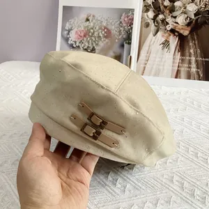 Detail of cream beret featuring subtle silver glitter and dual brown leather buckle straps