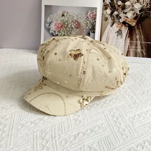 Close-up of beige newsboy hat with gold sequin embroidery and star patterns on cotton fabric