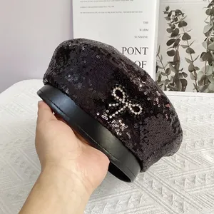 Détail d'un béret noir à paillettes avec un nœud en strass et bordure en similicuir