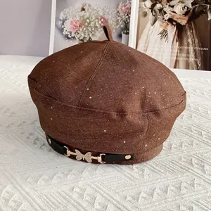 Close-up of brown denim beret featuring a golden butterfly rhinestone buckle and sequins