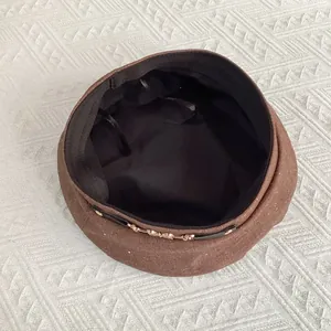 Detail view of brown beret showing interior lining, texture, and gold chain strap