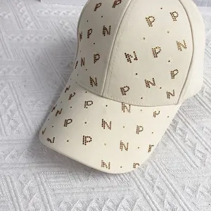 Détail de la casquette en toile beige avec lettres P et N étincelantes en strass