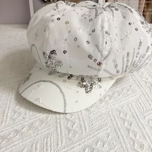 Close-up of sparkling silver sequins and star embroidery on white newsboy cap fabric