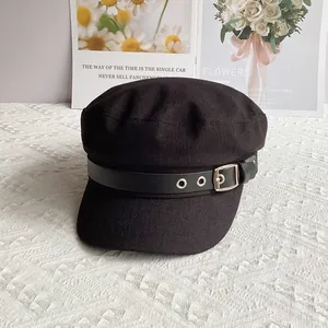Detail of black newsboy hat featuring textured fabric and faux leather strap with silver buckle