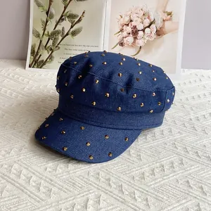 Detailed texture of blue denim newsboy hat with golden metal rivets on white knit background