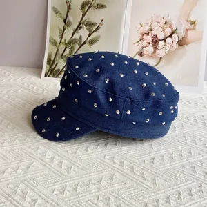 Detail of dark blue denim cadet cap featuring silver metallic rivets on a textured surface