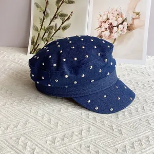 Detail of blue denim cadet cap with silver rivets on a white textured background