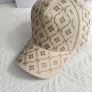 Détail d'une casquette beige avec motifs H en strass dorés et finitions cloutées chic