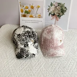 Detail of sequined baseball caps with floral patterns and gold bow accents on a mat