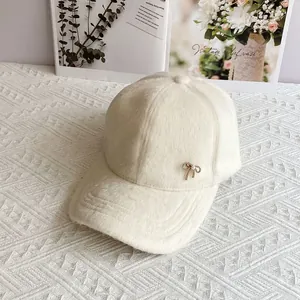 Dettaglio del cappellino in peluche bianco panna con fiocco dorato e perla sintetica