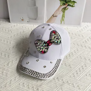 Detailed view of colorful rhinestone bow and silver studs on white denim baseball cap