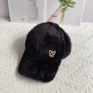 Detailed view of black faux fur baseball cap with metallic butterfly ornament on a knit mat