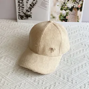 Dettaglio del berretto in peluche beige con un elegante ciondolo a fiocco dorato fine