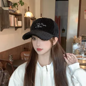 Detail of black corduroy baseball cap with white fashion embroidery in a cafe setting