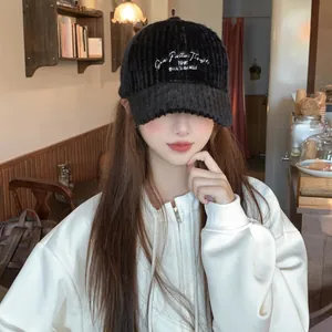 Fashionable black corduroy baseball cap with white embroidered letters in cozy cafe setting
