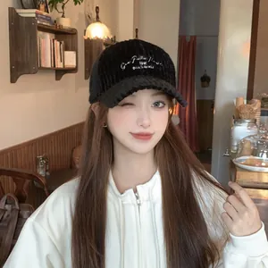 Detail of white embroidery text on a black corduroy baseball cap worn in a cafe setting