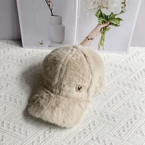 Detail of plush beige baseball cap featuring a golden butterfly metal logo and soft fur texture