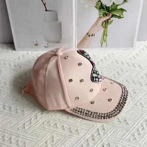 Detail of light pink denim cap featuring rhinestones and colorful gemstone butterfly