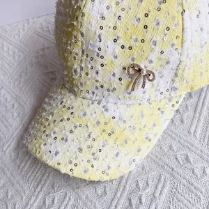 Close-up of baseball cap featuring silver sequins, frayed fabric, and a pearl bow detail