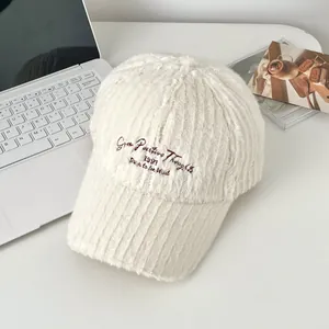 Close-up of white plush baseball cap with brown letter embroidery on a white desk