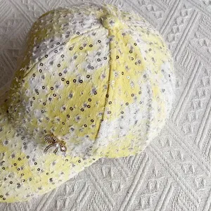 Detail of yellow plaid sequin baseball cap with pearl bow and distressed tweed texture