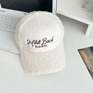 Close-up of beige faux fur baseball cap with red embroidered letters in cozy home setting