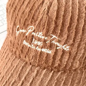 Detailed close-up of brown plush baseball cap with white embroidered positive quotes