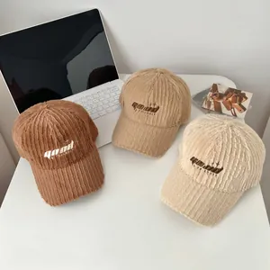 Three embroidered plush baseball caps in brown, camel and beige on a clean desk