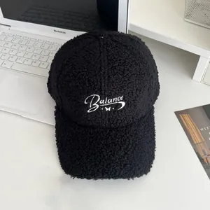 Detail of black faux shearling baseball cap with Balance embroidery on laptop desk