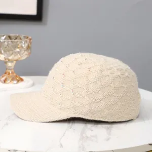 Detail of beige knitted baseball cap with sparkling colorful rhinestones on marble surface