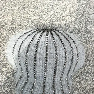 Dettaglio del berretto in maglia grigio chiaro con decorazioni radiose di strass scuri
