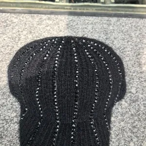 Dettaglio del berretto in maglia nera con strass verticali e una morbida trama di pelliccia