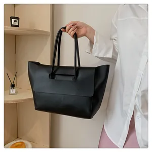 Detail of a large black matte tote bag with slim handles and a unique folding flap closure