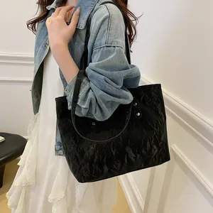 Large black tote bag with glossy wrinkled texture and shoulder straps on a casual model