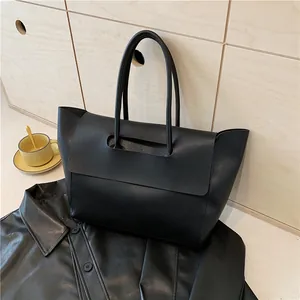 Large black leather tote bag with unique flap handle design on wooden background