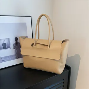 Minimalist beige leather wing tote bag with a unique cutout handle on a black cabinet