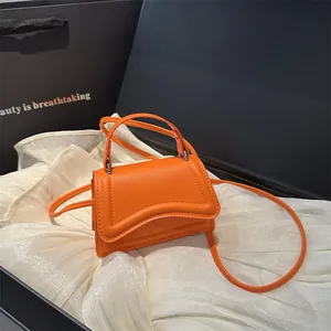 Mini oranje crossbodytas met golvende flap op elegante witte zijden achtergrond