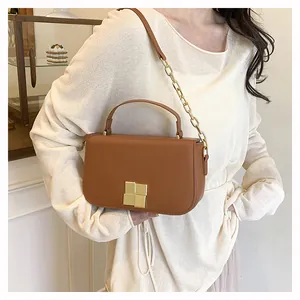 Detail van een bruine leren crossbodytas met gouden ketting en vierkante metalen gesp