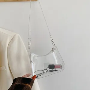 Macro detail of clear PVC crescent shoulder bag showing silver hardware and inner items
