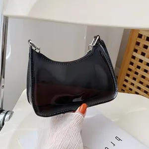 Glossy black patent leather crescent shoulder bag with silver hardware on white chair
