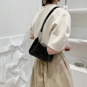 Glossy black patent leather shoulder bag with sleek silver hardware shown on a model