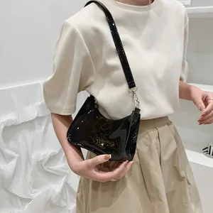 Model wearing a glossy black patent leather underarm shoulder bag with a sleek finish