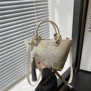 Chic beige bucket bag with gold bamboo pattern and elegant bead tassel decoration