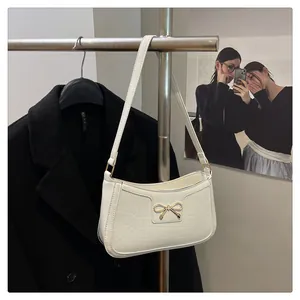 Detail der weißen Schultertasche mit Krokodilmuster und dekorativem goldfarbenem Bogen