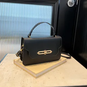 Classic black leather handbag with gold metal lock and shoulder strap on beige books
