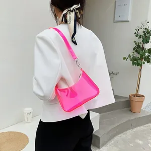 Detail view of a neon pink transparent PVC underarm bag worn with a white blazer
